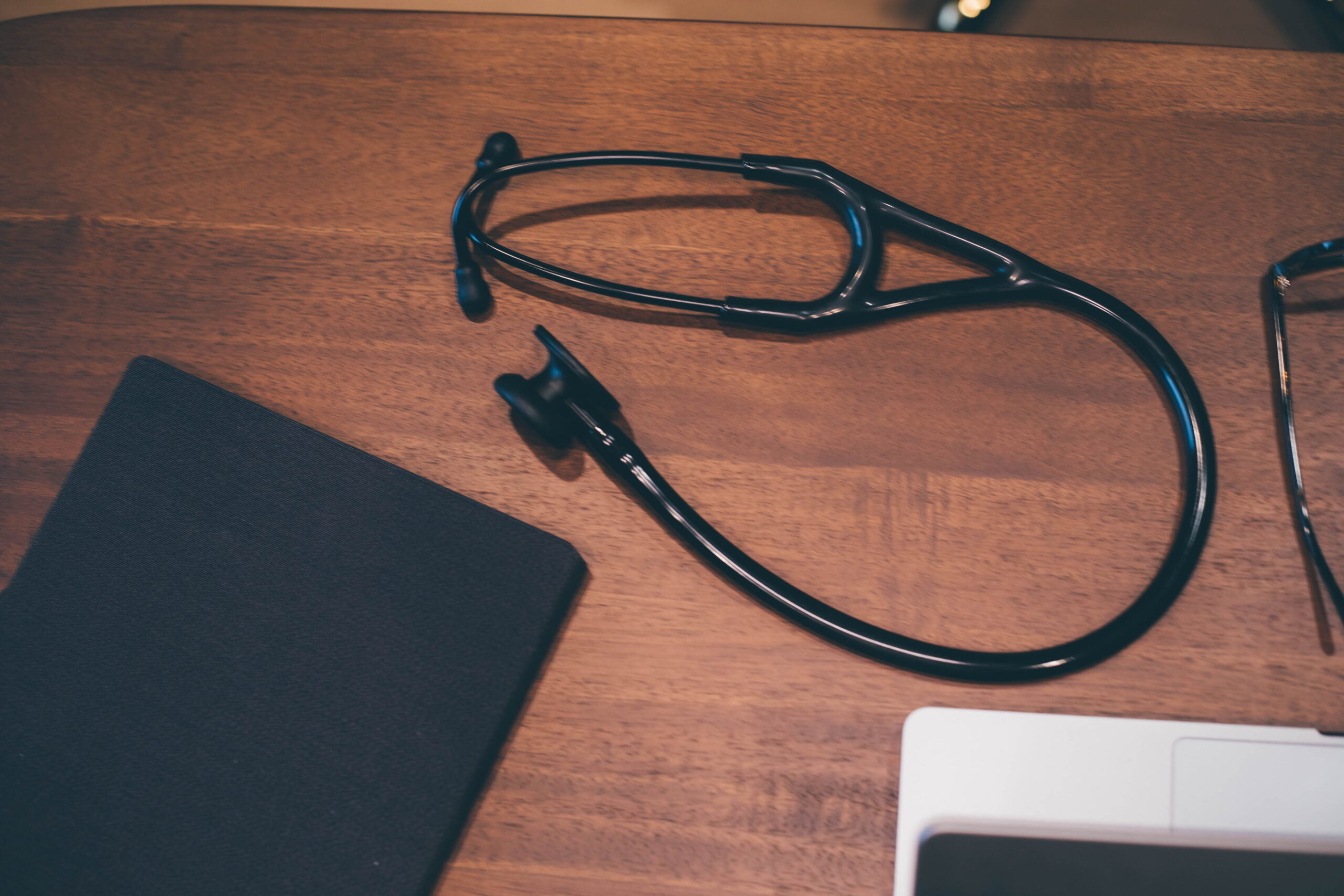 A black stethoscope and medical documents on a dark wooden desk.