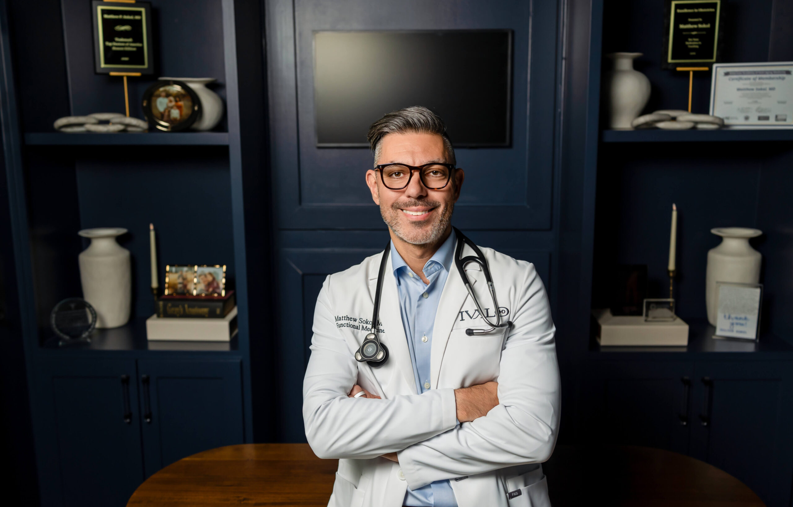 Dr. Sokol in a navy suit with a stethoscope, seated against a dark backdrop